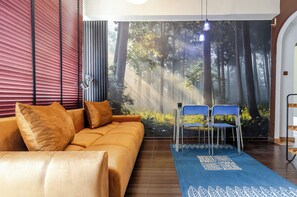 Ein modernes Wohnzimmer mit einer Couch, zwei Sesseln, einem blauen Teppich und einer Waldlandschaft an der Wand.
