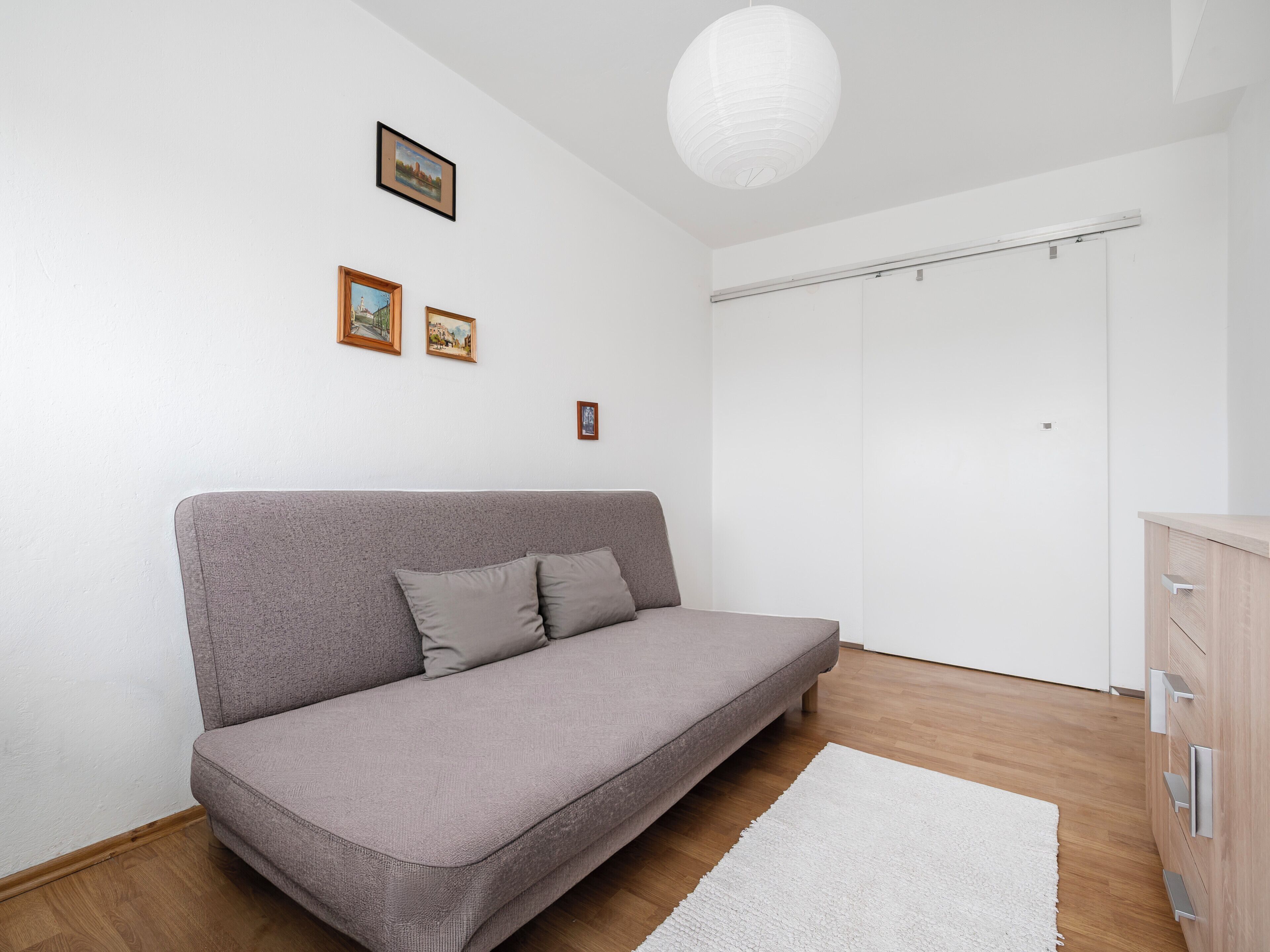 Una habitación moderna con un sofá gris, una lámpara de techo blanca y suelo de madera.