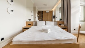 Ein modernes Hotelzimmer mit einem großen Bett, einem Holzkopfteil, Nachttischen, einem Kleiderschrank und einem großen Fenster mit Vorhängen.