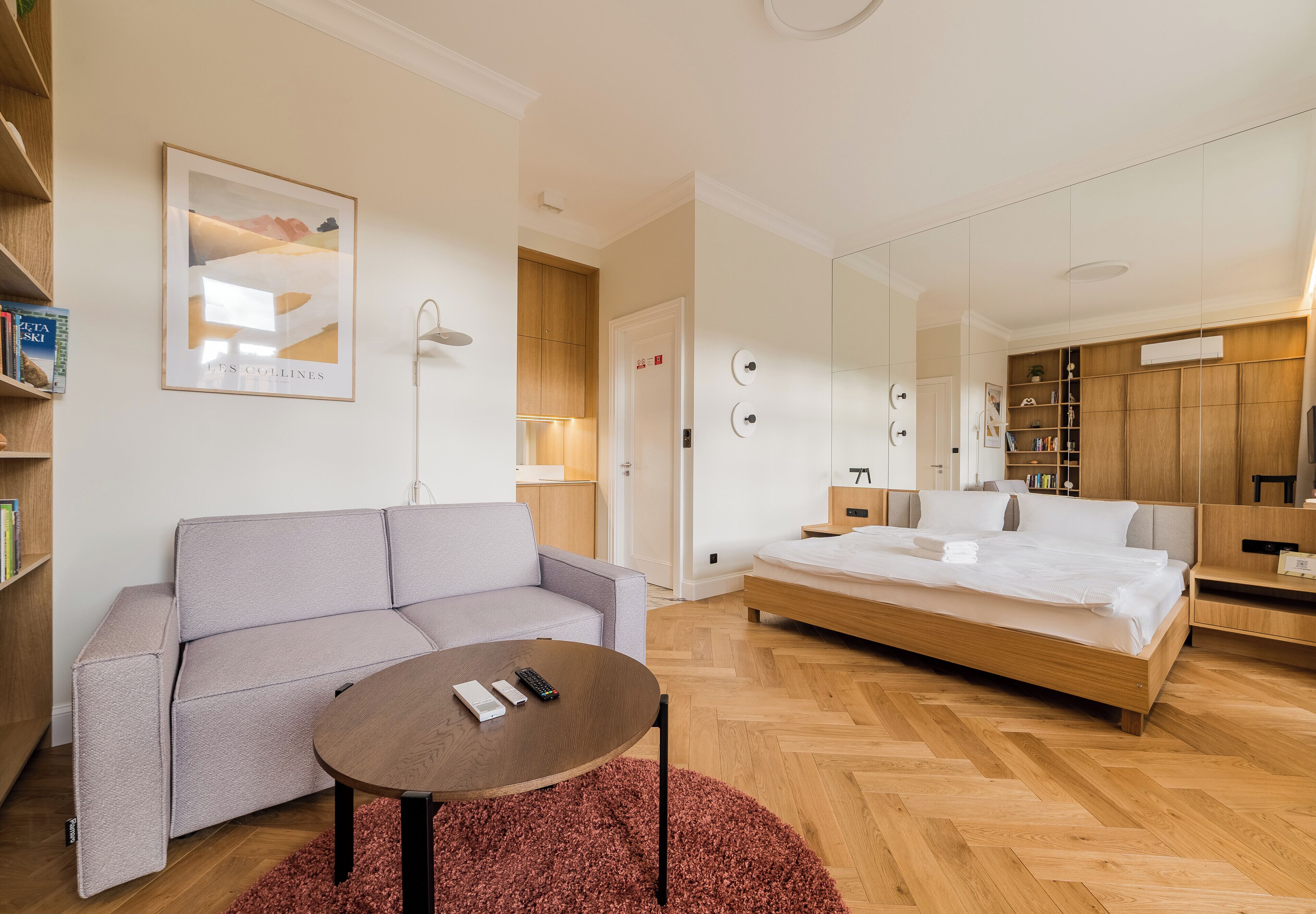 Een moderne hotelkamer met een bank, een ronde tafel, een bed, een spiegel en een boekenplank.