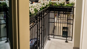Ein Balkon mit weißen Blumen, einem schwarzen Metallgeländer und Gebäuden im Hintergrund.