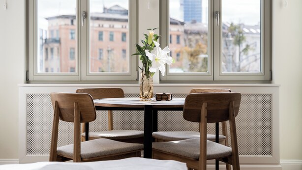 Ein Esstisch mit vier Stühlen, eine Vase mit Blumen und ein Fenster mit Blick auf die Stadt.