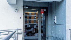 Rakennuksen sisäänkäynti, jossa on lasiovi, metallinen numerokilpi ja palohälytysjärjestelmä.