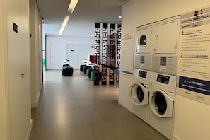 Corredor de hotel com máquina de lavar, área de estar e uma porta no final.