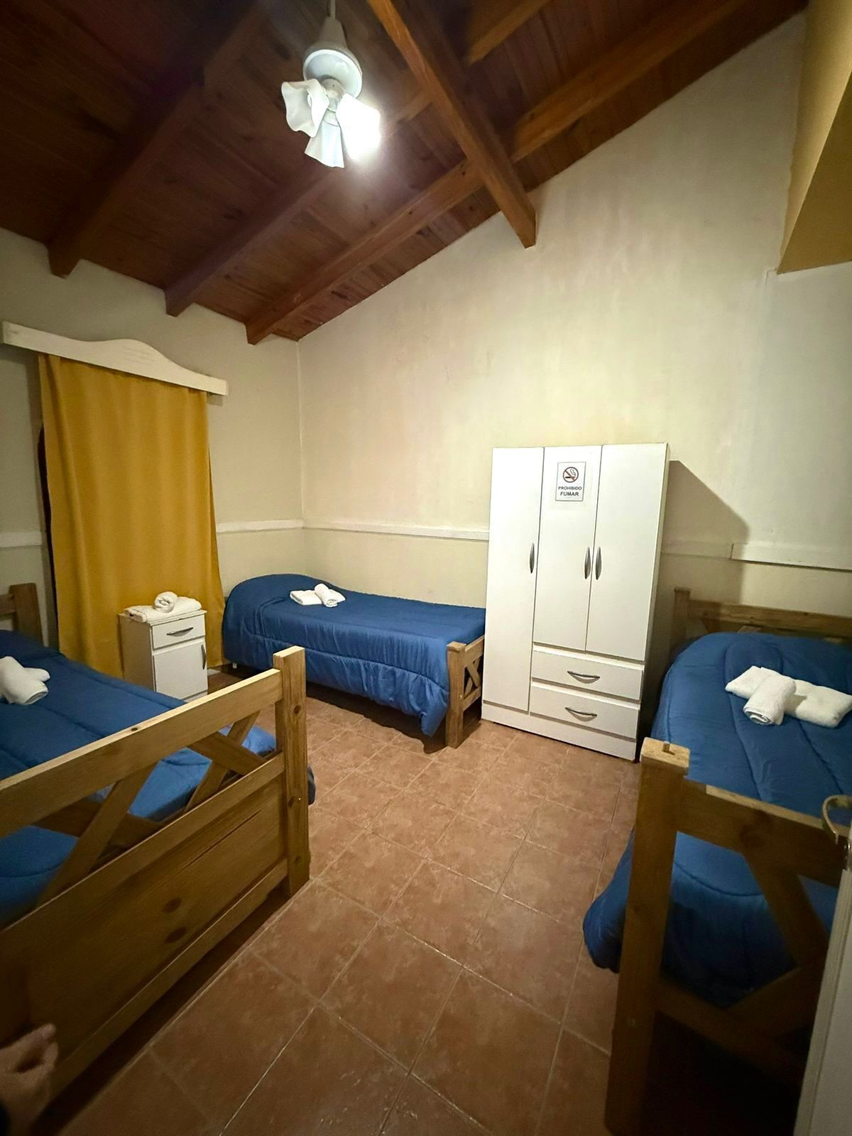 Een kamer met twee houten bedden, een witte kledingkast, een klein bureau en een plafondventilator.