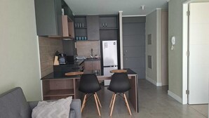 Eine kleine Küche mit Kühlschrank, Spüle und einer Essecke mit zwei Stühlen.