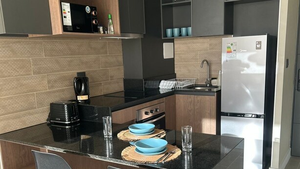 Eine moderne Küche mit einer zentralen Kochinsel, zwei Stühlen, einem Kühlschrank und einer Mikrowelle.