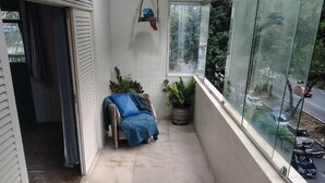 Ein Balkon mit Tisch, zwei Hockstühlen, einer Topfpflanze und einem blauen Stuhl.