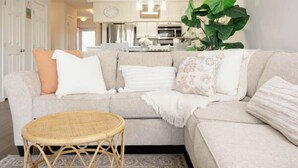 A living room with a sofa, a round wicker table, and a large plant. - Tee Time Retreat- Pool Access + Premier Golf (Myrtle Beach)
