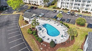 A hotel with a swimming pool, parking lot, and a building with multiple floors. - Tee Time Retreat- Pool Access + Premier Golf (Myrtle Beach)