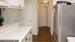 A kitchen with white cabinets, a stainless steel refrigerator, and a wooden floor. - Tee Time Retreat- Pool Access + Premier Golf (Myrtle Beach)