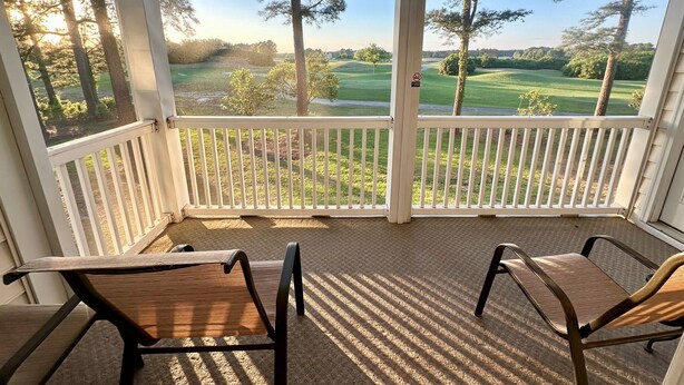 A covered porch with two chairs, a view of a golf course, and a no-smoking sign. - Tee Time Retreat- Pool Access + Premier Golf (Myrtle Beach)