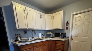 Una cocina con armarios blancos, una mesa de madera, un microondas, un tostador y una tetera.