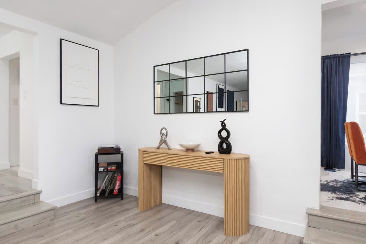 Ein modernes Wohnzimmer mit einem Holztischchen, einem Spiegel mit schwarzem Rahmen und einem schwarzen Bücherregal.