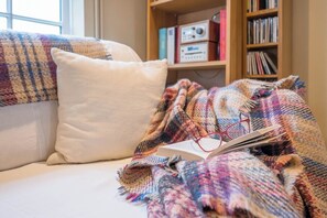 Ein gemütliches Zimmer mit einem Bett, einer bunten Decke, einem Kissen und einem Bücherregal mit Büchern und einem Radio.