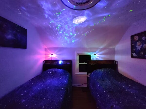 A room with two single beds, a ceiling fan, and a wall-mounted shelf.