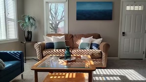 En stue med sofa, sofabord, en potteplante og et billede på væggen.