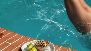 Angolo a bordo piscina con un piatto di frutta secca e due bicchieri di liquido ambrato, probabilmente una bevanda.