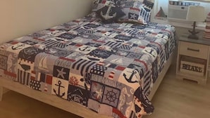Quarto com cama, mesa de cabeceira, janela com persianas e espelho fixado na parede.