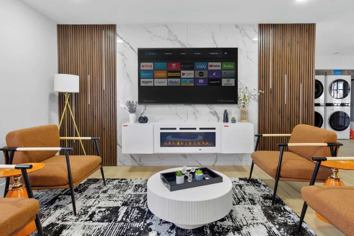 Uma sala de estar moderna com uma televisão de tela plana na parede, dois sofás, uma mesa de centro, um abajur e uma lareira.
