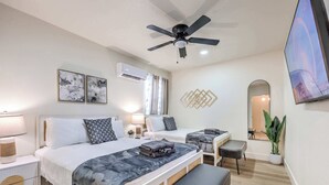 Ein modernes Hotelzimmer mit zwei Betten, einem Deckenventilator, einer Klimaanlage, einem Fernseher, einem Spiegel und einer Topfpflanze.