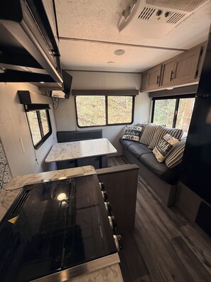 A compact RV kitchen with a stove, a countertop, and a seating area with a window view.