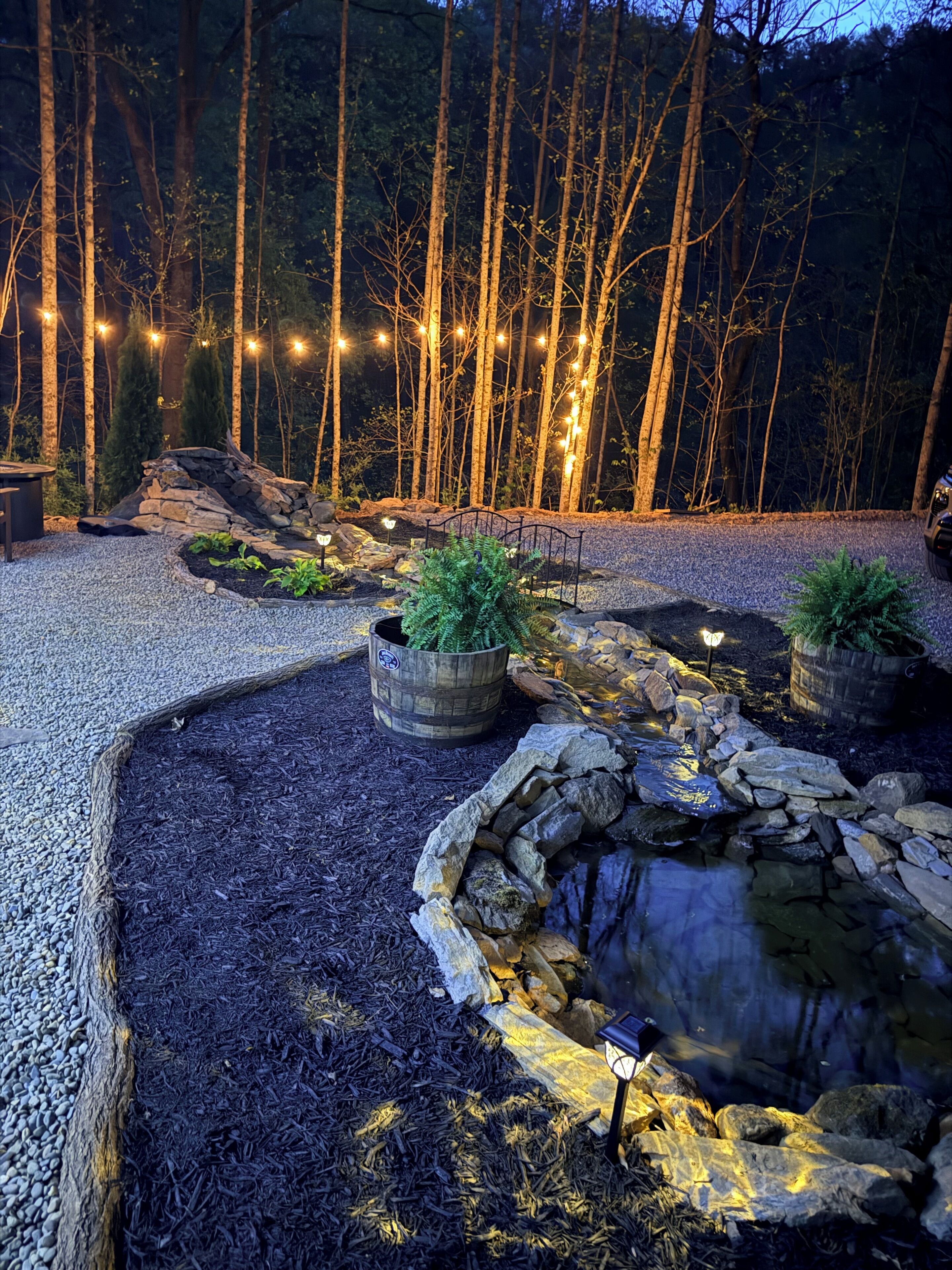 A landscaped garden with a pond, stone walls, and string lights.