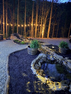 A landscaped garden with a pond, stone walls, and string lights.
