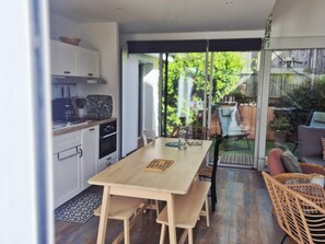 A modern kitchen with white cabinets, a wooden dining table, and a view of a garden through glass doors. - Modern house in a quiet location near downtown and the beaches (FOURAS)