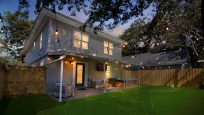A two-story house with a patio area, a lawn, and string lights. - Coastal Clubhouse | Hot Tub, Game Room & Pet-Friendly Vacation Home (Saint Simons Island)