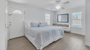 A bedroom with a bed, a ceiling fan, a window, and a door. - Coastal Clubhouse | Hot Tub, Game Room & Pet-Friendly Vacation Home (Saint Simons Island)