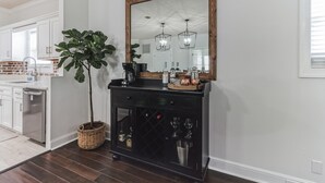 A kitchen with white cabinets, a black countertop, a large mirror, and a potted plant. - Coastal Clubhouse | Hot Tub, Game Room & Pet-Friendly Vacation Home (Saint Simons Island)