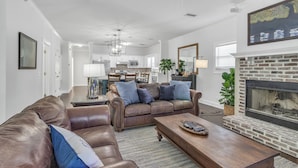 A living room with a fireplace, leather sofas, a coffee table, and a dining area in the background. - Coastal Clubhouse | Hot Tub, Game Room & Pet-Friendly Vacation Home (Saint Simons Island)