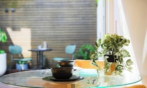 Ein Glastisch mit einer schwarzen Schale und Untertasse, einem Blumentopf und Blick auf eine Ziegelwand und einen Außenbereich mit Sitzgelegenheiten.