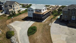 Ett bostadsområde med hus som ligger nära en strand, med ett stort hus som har en balkong och ett mindre hus med en veranda.