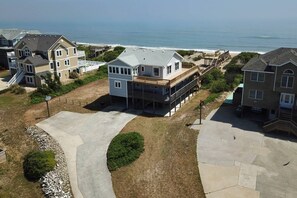 A residential area with houses near a beach, featuring a large house with a balcony and a smaller house with a deck. - Anna - Corolla, Ocean Sands, Oceanfront, 4 Bedrooms, Ocean Views, Private Walkway to the Beach (Corolla)