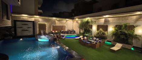 Un área de piscina con jacuzzi, asientos y un patio bien iluminado.