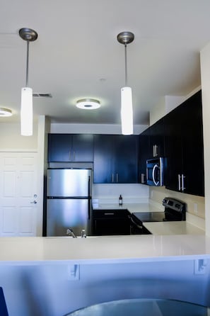 A modern kitchen with stainless steel appliances, dark cabinetry, and pendant lighting.