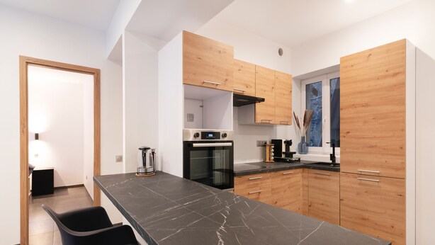 Een moderne keuken met een marmeren aanrecht, houten keukenkastjes en een inbouwoven.