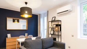 Een moderne woonkamer met een bank, een eettafel, stoelen, een hanglamp, een spiegel en een boekenkast.