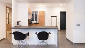 Een moderne keuken met een marmeren aanrechtblad, twee zwarte barkrukken en een klok aan de muur.