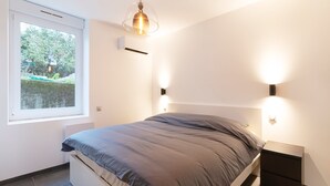 Een slaapkamer met een bed, een raam, een wandairconditioner en een hanglamp.