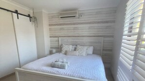 Ein Schlafzimmer mit einem Bett, einem Deckenventilator, einem Fenster mit Jalousien und einer Wand-Klimaanlage.