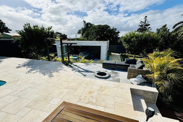 Un patio trasero con piscina, mobiliario exterior y un pérgola.