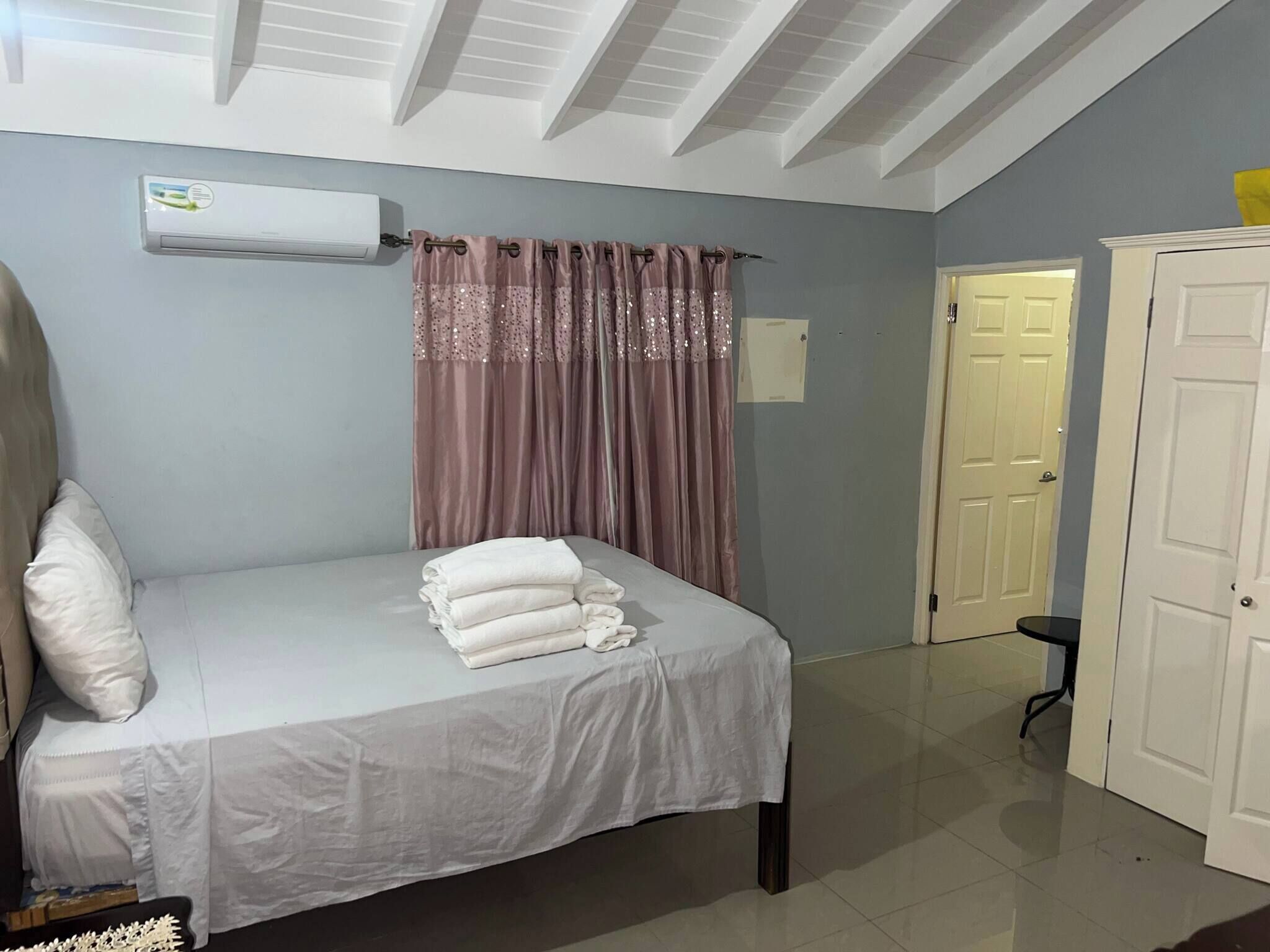 A bedroom with a bed, a white air conditioning unit, a door, and a chair.