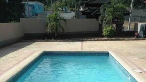 Una piscina rectangular con agua azul cristalina, rodeada por un borde de baldosas.
