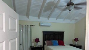 Un dormitorio con cama, dos mesitas de noche, ventilador de techo, aire acondicionado y ventana con cortinas.
