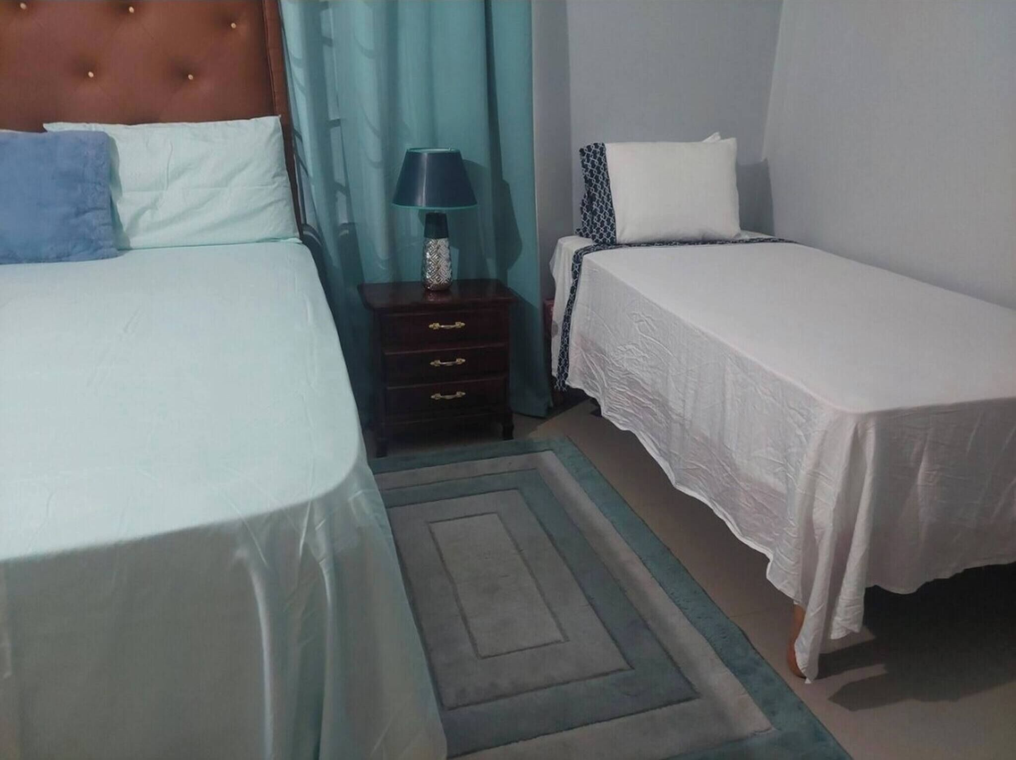 A bedroom with two beds, a nightstand, a lamp, and a patterned rug.