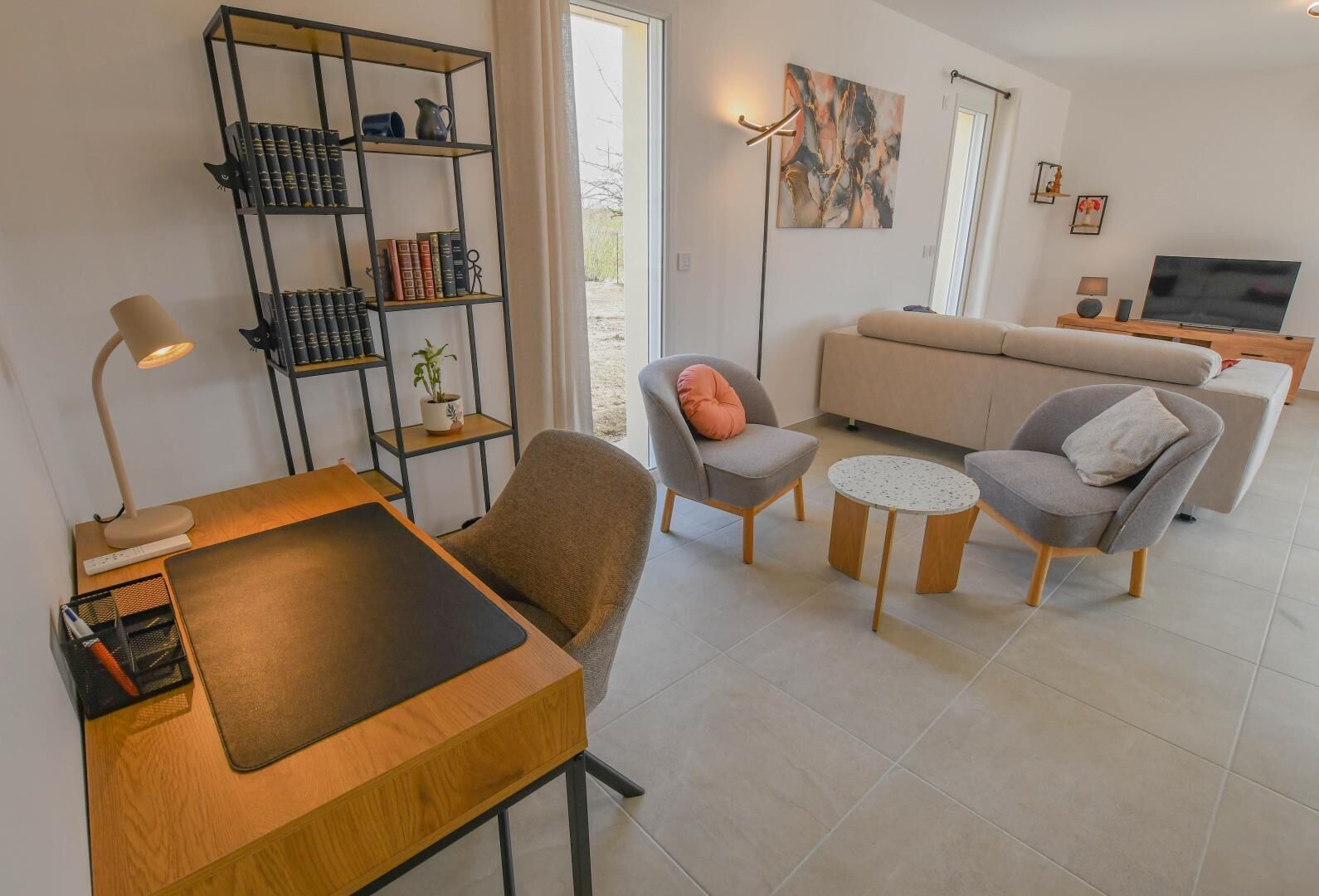 Un salon moderne comprenant un canapé, deux fauteuils, une table basse, une bibliothèque, un bureau avec une lampe et un téléviseur.