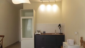 A compact kitchen with a white refrigerator, dark cabinets, a countertop with a toaster, and a small table with a lamp. - balcony  Studio (Thành phố Hồ Chí Minh)